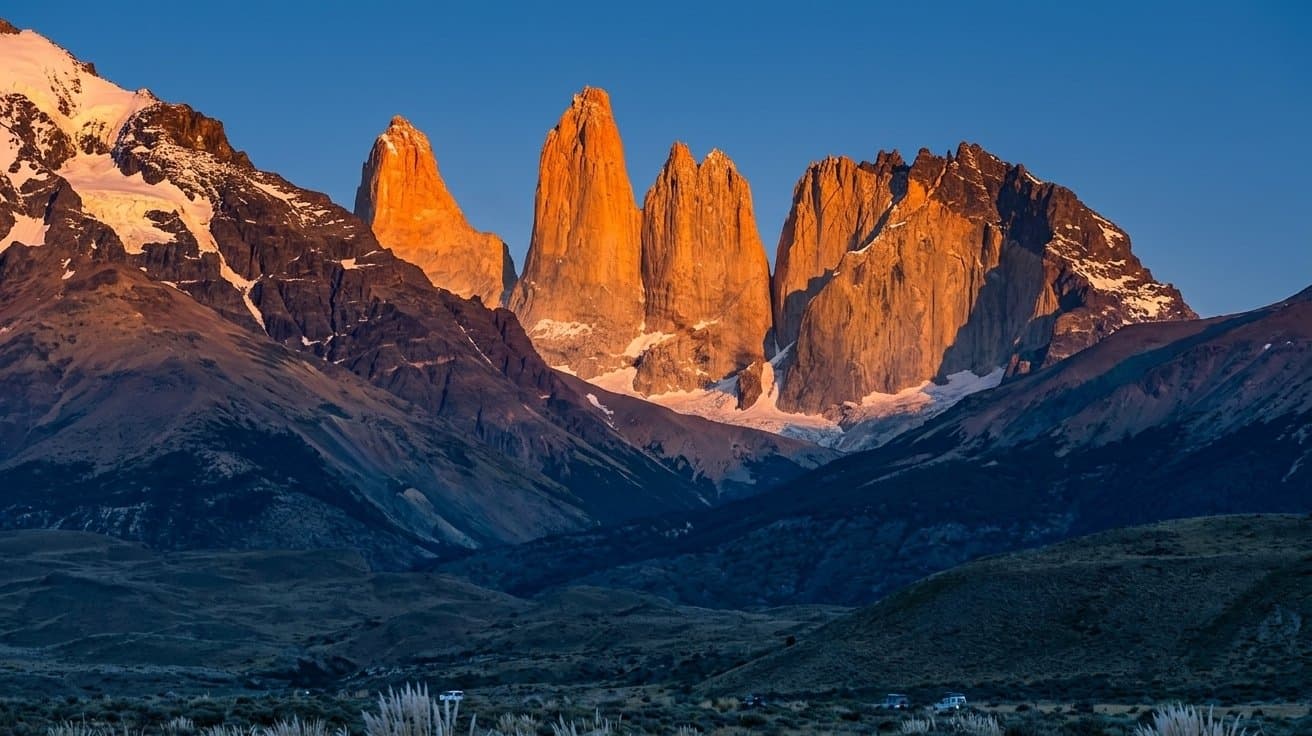The granite towers of Torres del Paine in Chilean Patagonia lit orange at sunrise above the valley