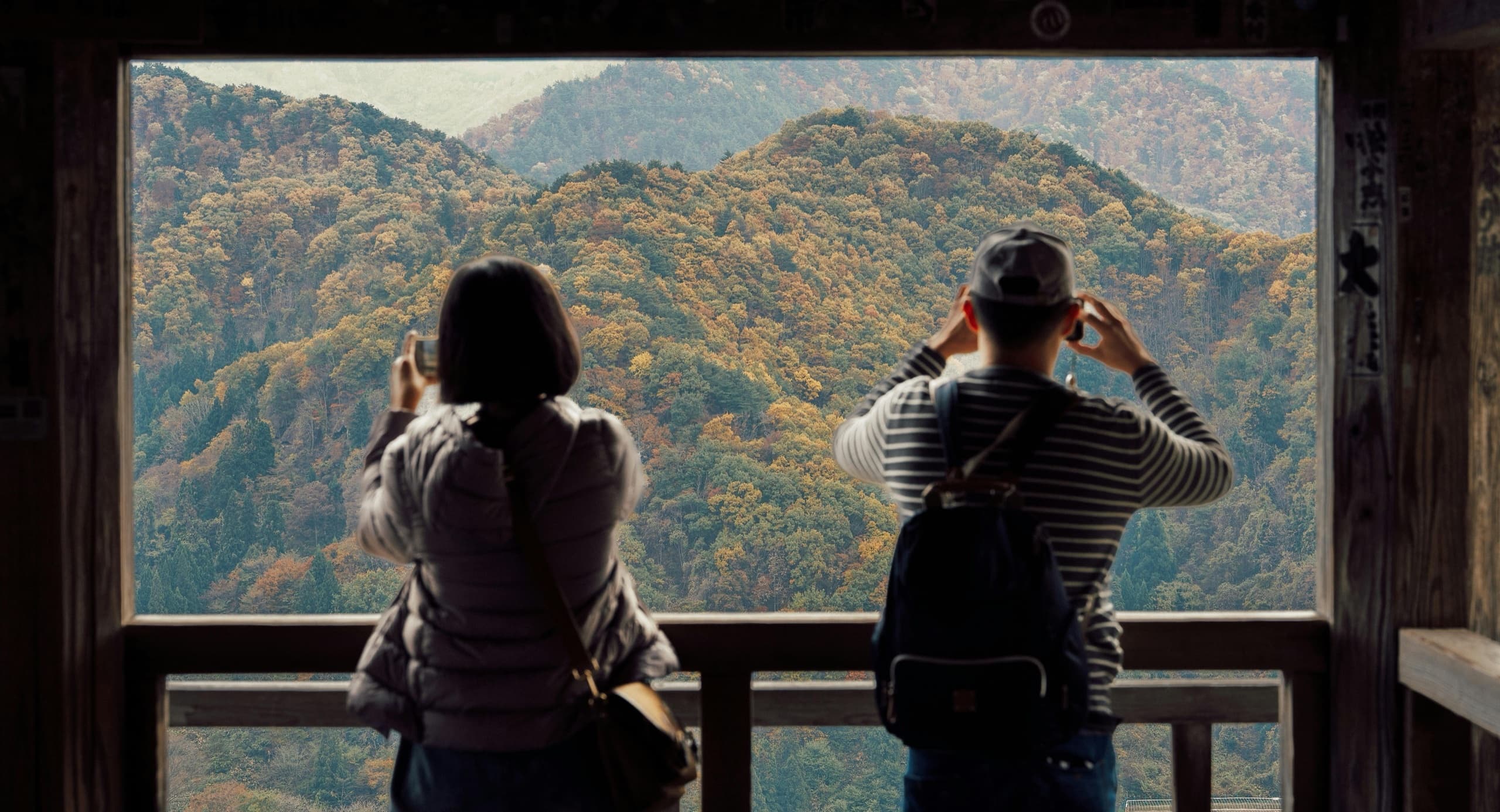 Travelers photographing autumn mountains from a Japanese temple viewpoint