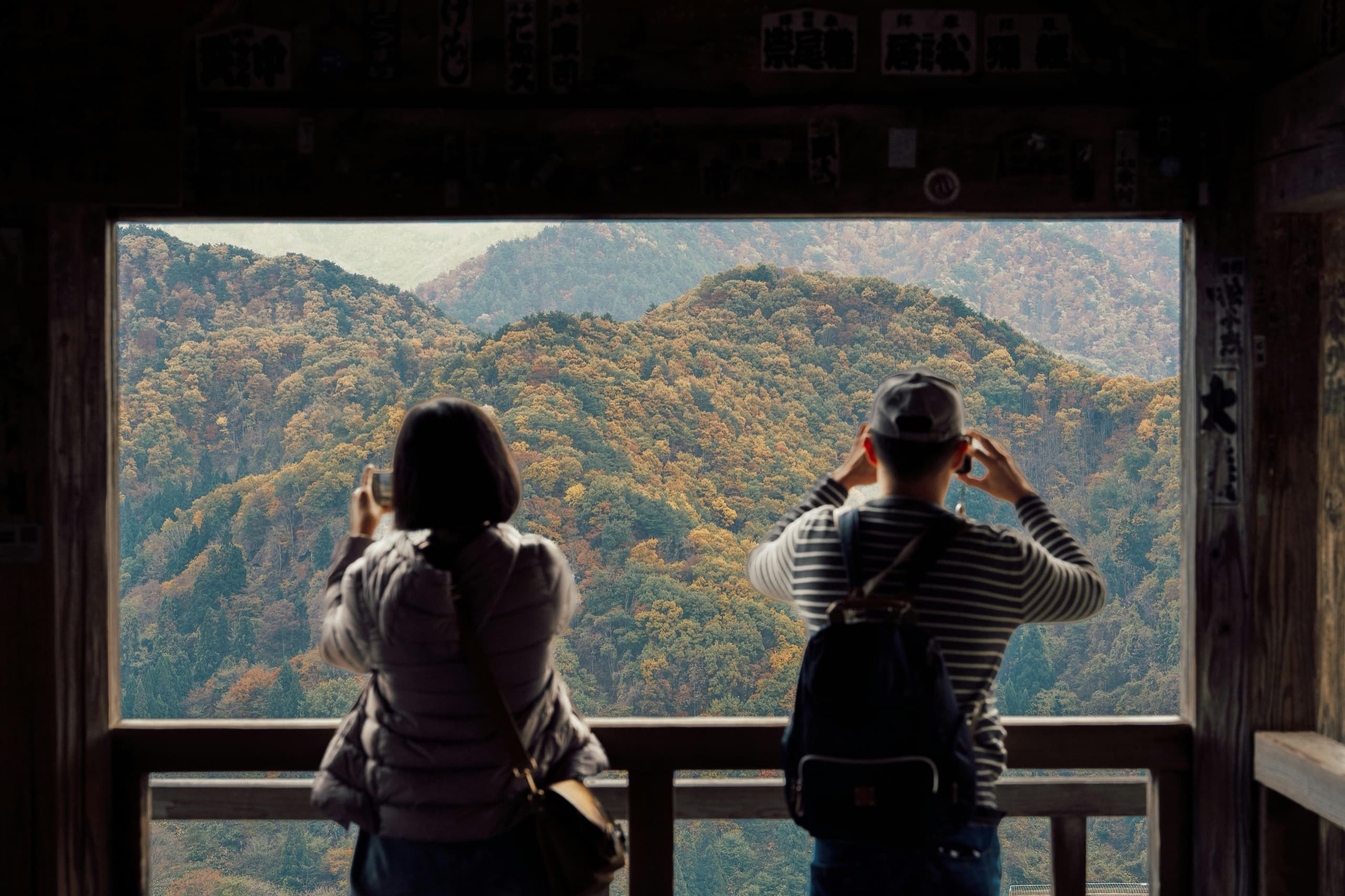 Travelers photographing autumn mountains from a Japanese temple viewpoint