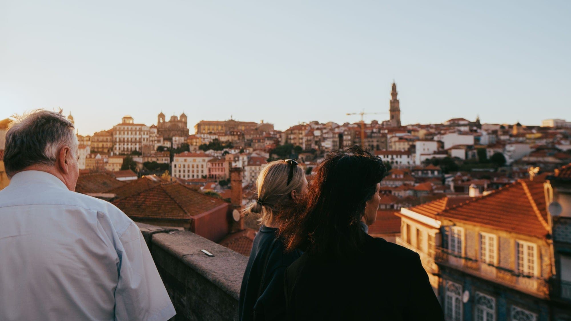Three travellers on a terrace above Porto at sunset, looking out over the tiled rooftops and the Clérigos tower