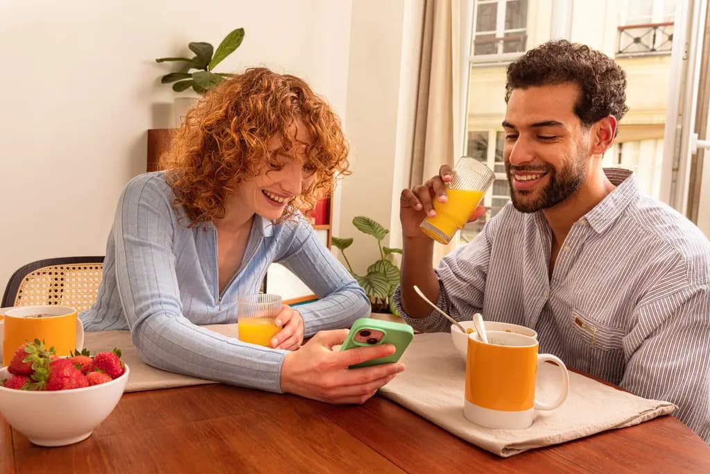Couple smiling while looking at a smartphone during breakfast